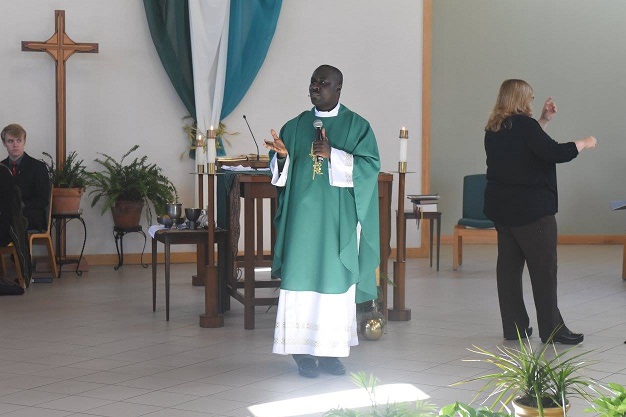 Father Mark giving homily in front of alter with sign language interpreter on the side.