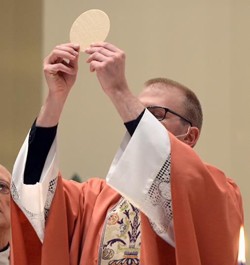 Father Ryan Andrew holds up the Eucharist